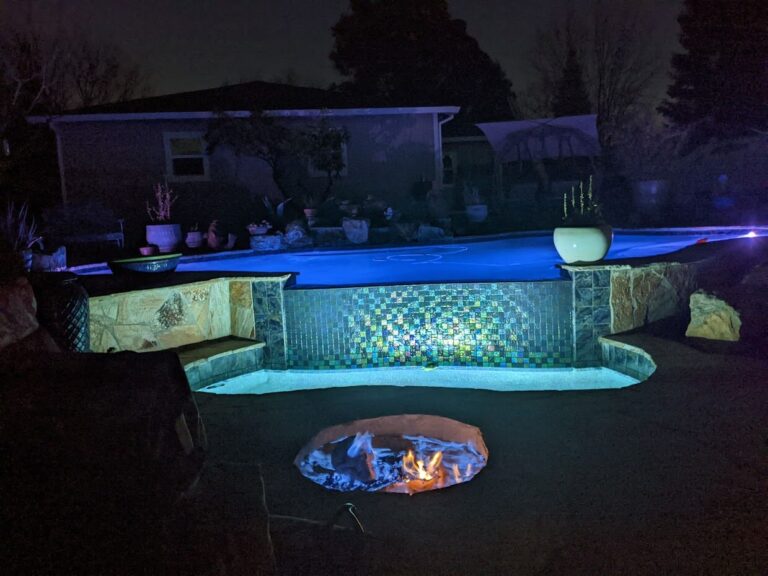 Pool at night and night lights next to firepit.