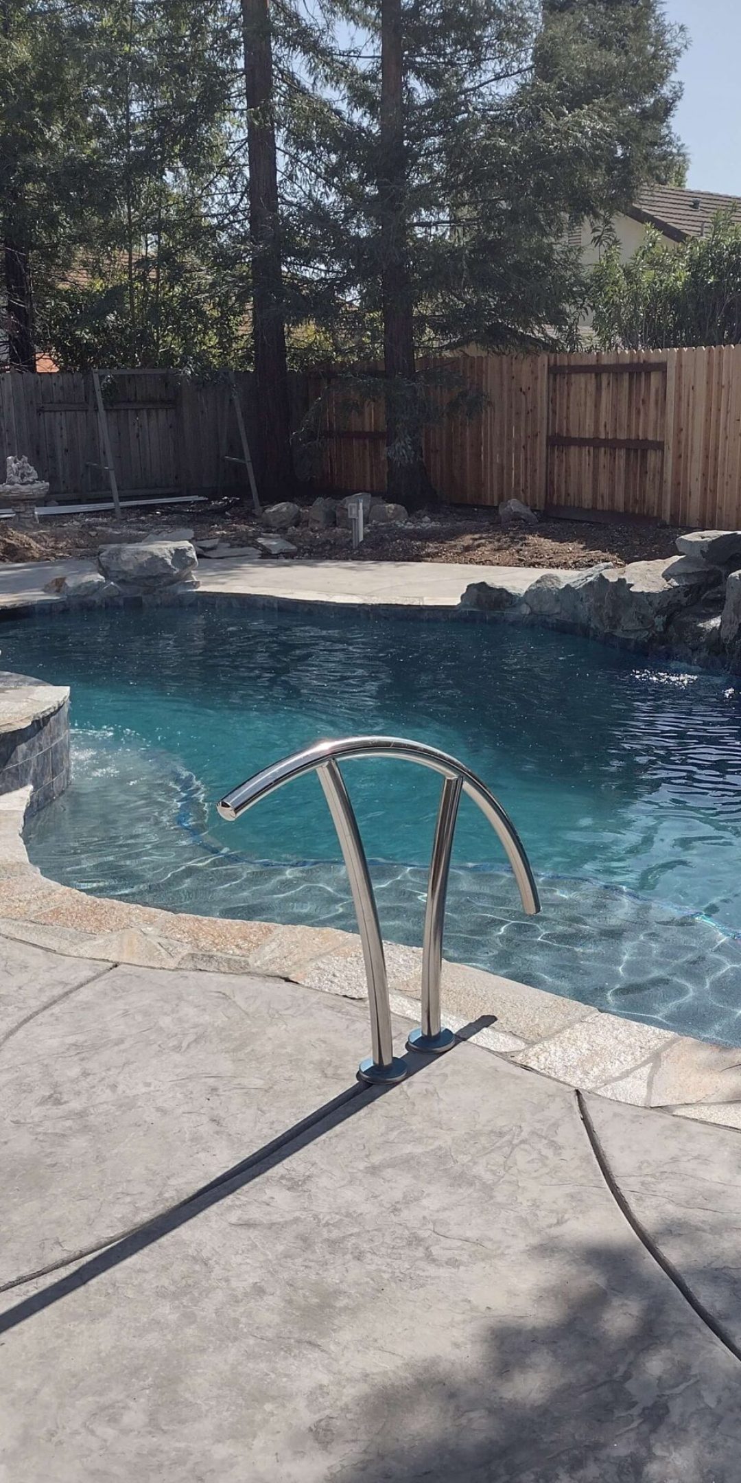 freeform pool with natural rock waterfall, bubbling spa, and silver handrail into the pool